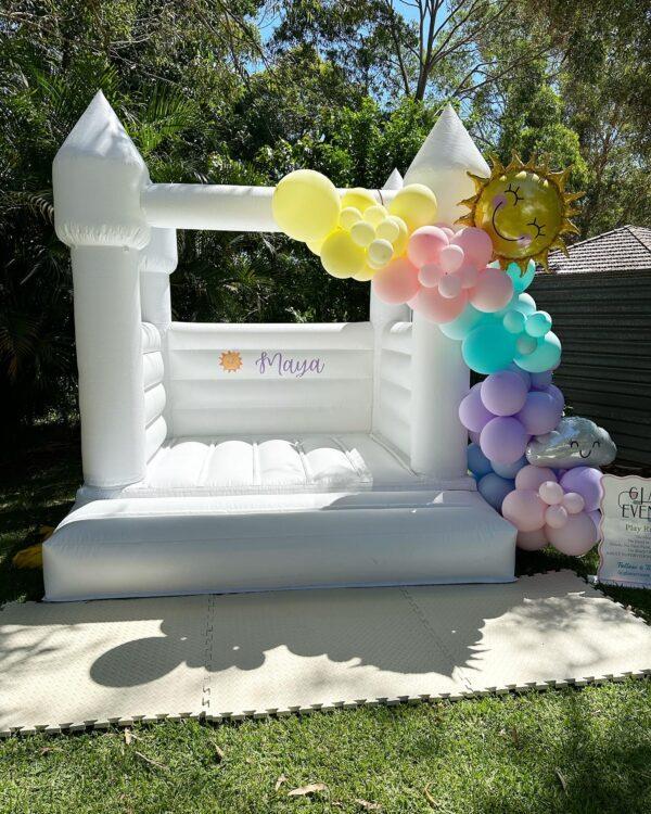 small white jumping castle with a balloon arch.